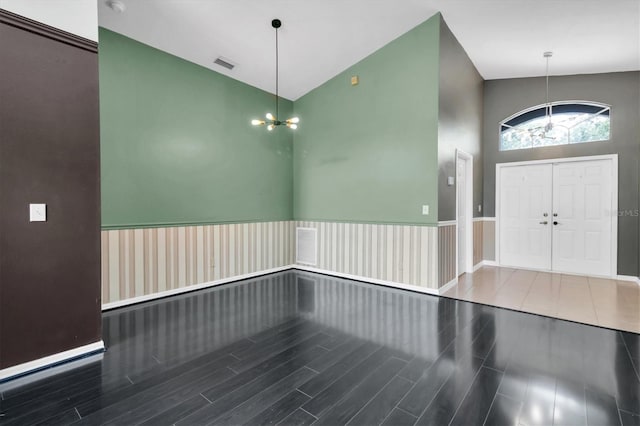 foyer entrance featuring high vaulted ceiling, wood finished floors, visible vents, and an inviting chandelier