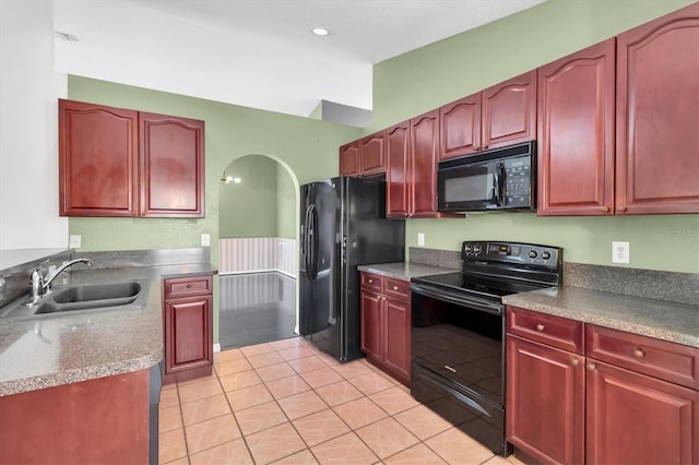 kitchen featuring reddish brown cabinets, arched walkways, light tile patterned floors, a sink, and black appliances