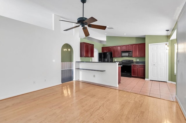 kitchen with ceiling fan, arched walkways, light wood-type flooring, reddish brown cabinets, and black appliances