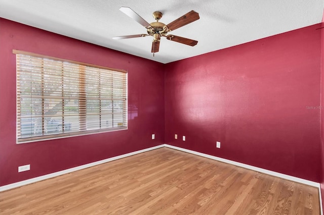 empty room with ceiling fan, a textured ceiling, baseboards, and wood finished floors