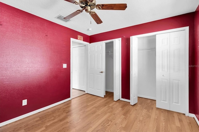 unfurnished bedroom with multiple closets, visible vents, ceiling fan, wood finished floors, and baseboards