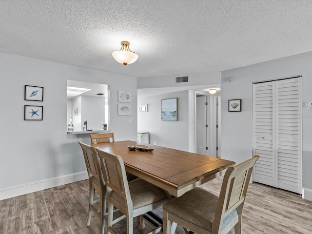 dining area with light wood-type flooring, a textured ceiling, and sink