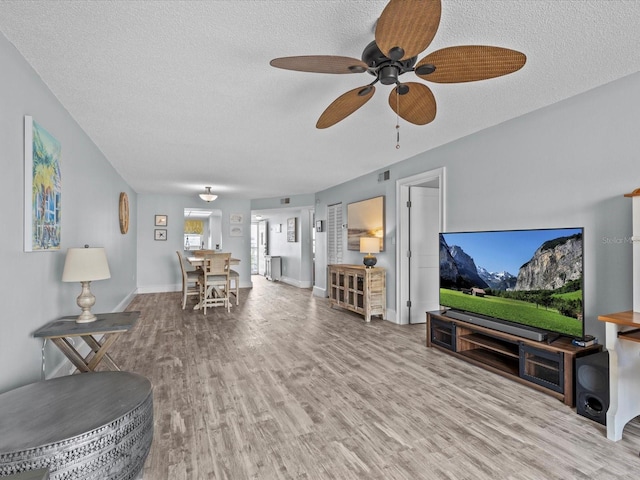 living room with ceiling fan, a textured ceiling, and light hardwood / wood-style flooring