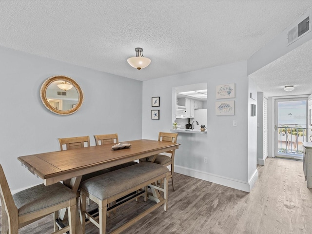 dining room with a textured ceiling, sink, and light hardwood / wood-style floors