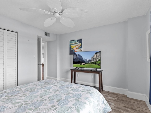 bedroom with hardwood / wood-style floors, ceiling fan, a closet, and a textured ceiling