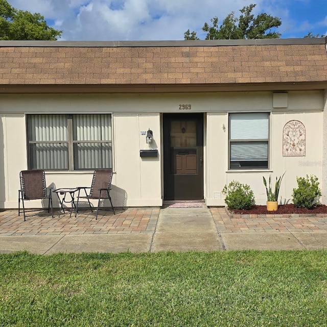 view of exterior entry featuring a shingled roof, a patio area, and stucco siding