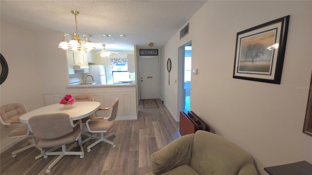 dining area with a textured ceiling, baseboards, visible vents, and light wood-style floors