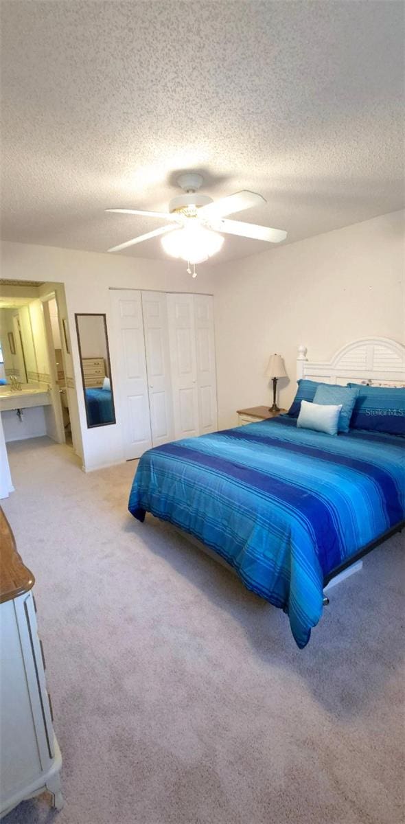 bedroom with a textured ceiling, a closet, ceiling fan, and light colored carpet