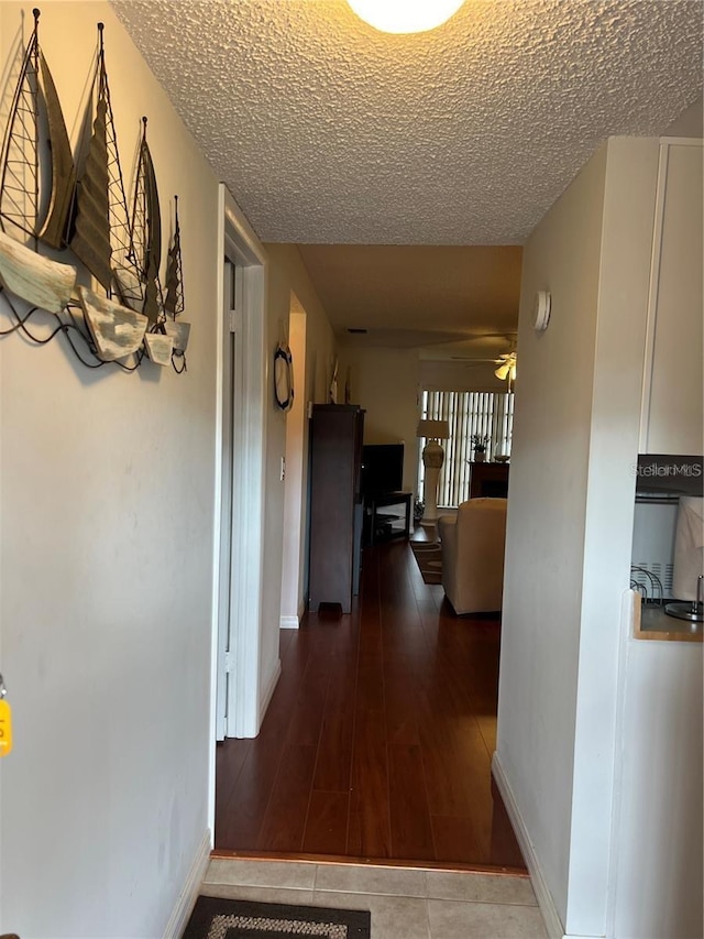 hallway with tile patterned flooring, baseboards, and a textured ceiling