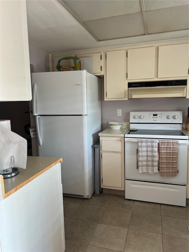 kitchen featuring dark tile patterned flooring, white appliances, cream cabinets, and a drop ceiling