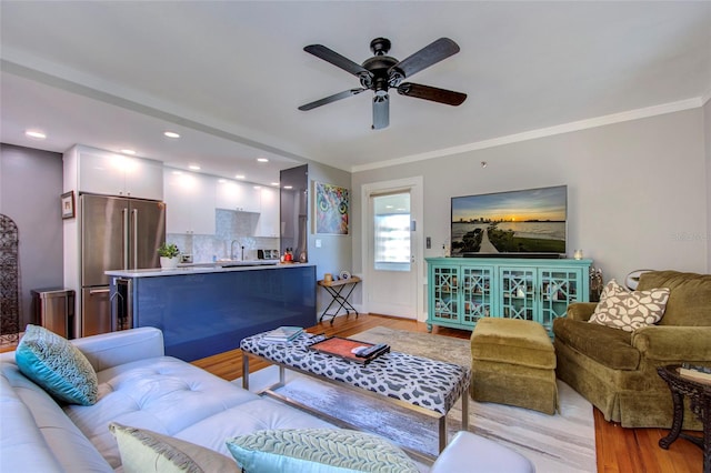 living room with ceiling fan, sink, light wood-type flooring, and crown molding