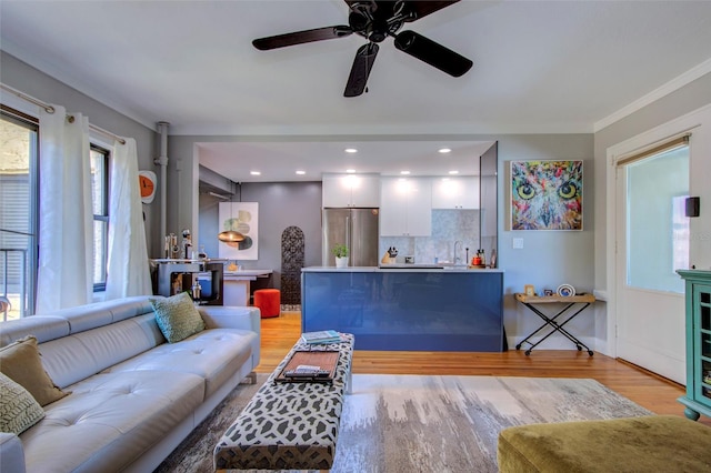 living room featuring light hardwood / wood-style flooring, ceiling fan, crown molding, and sink