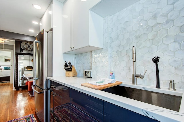 kitchen featuring stainless steel refrigerator, white cabinetry, light stone countertops, backsplash, and light hardwood / wood-style flooring