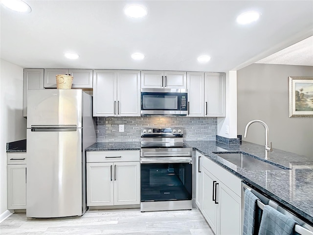 kitchen with dark stone countertops, backsplash, light wood-type flooring, appliances with stainless steel finishes, and sink