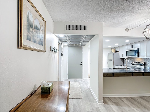 hall with a textured ceiling, sink, and light hardwood / wood-style floors