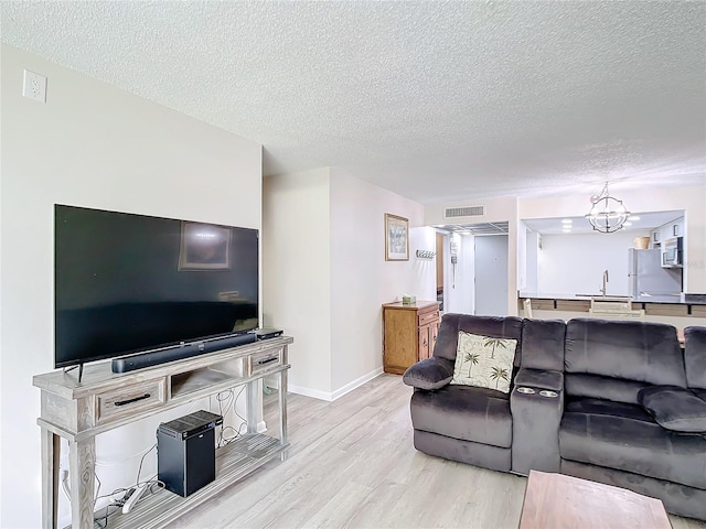 living room featuring a textured ceiling, an inviting chandelier, sink, and light hardwood / wood-style floors