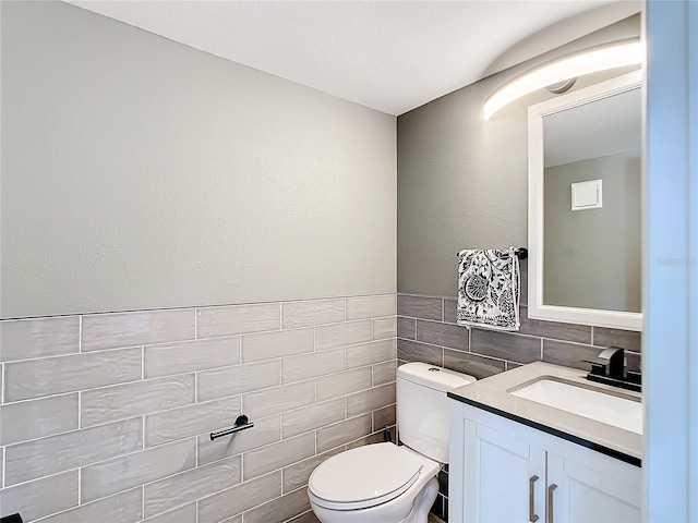 bathroom featuring vanity, toilet, backsplash, and tile walls