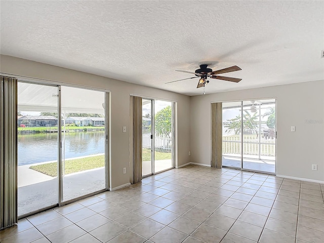 unfurnished room with a textured ceiling, ceiling fan, a water view, and light tile patterned floors