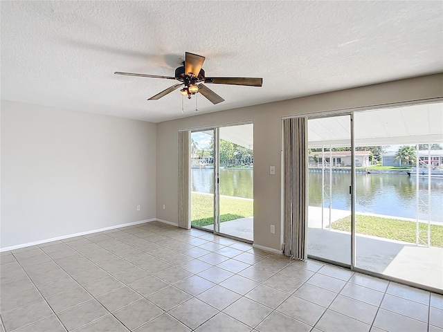 tiled spare room featuring ceiling fan, a water view, and a textured ceiling