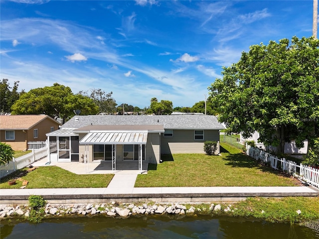 rear view of property with a sunroom, a water view, a yard, and a patio