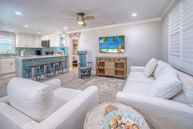 living room with baseboards, ceiling fan, crown molding, and light wood finished floors