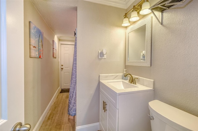 bathroom with baseboards, toilet, ornamental molding, wood finished floors, and vanity