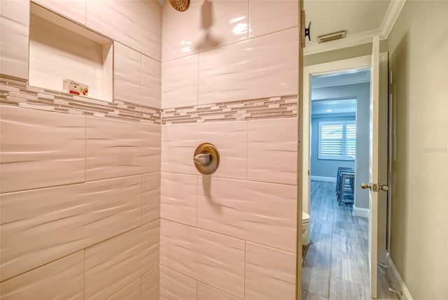 bathroom featuring toilet, wood finished floors, baseboards, and a tile shower