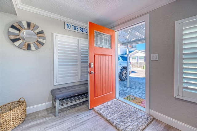 foyer entrance with baseboards, a textured ceiling, wood finished floors, and crown molding