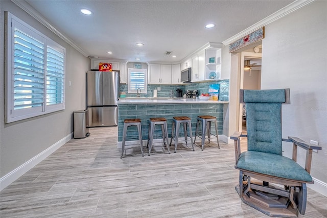 kitchen featuring a peninsula, appliances with stainless steel finishes, white cabinetry, a kitchen breakfast bar, and tasteful backsplash