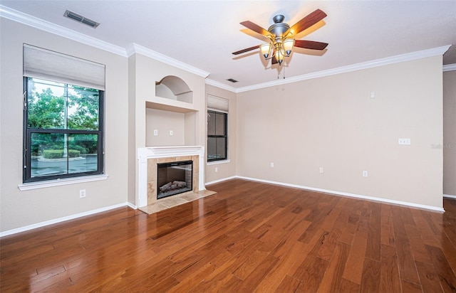 unfurnished living room featuring built in features, a tiled fireplace, ceiling fan, hardwood / wood-style flooring, and ornamental molding