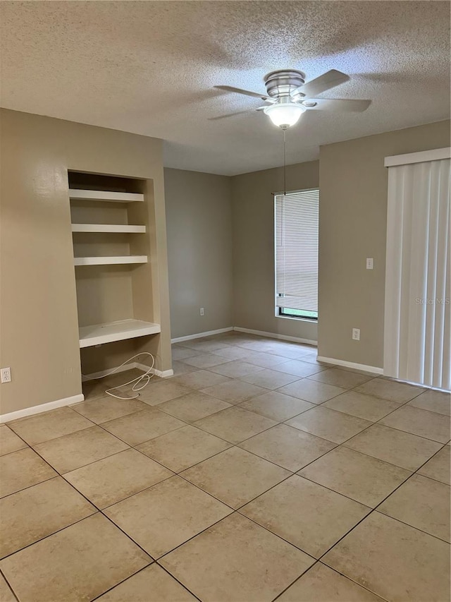 tiled empty room with built in shelves, ceiling fan, and a textured ceiling