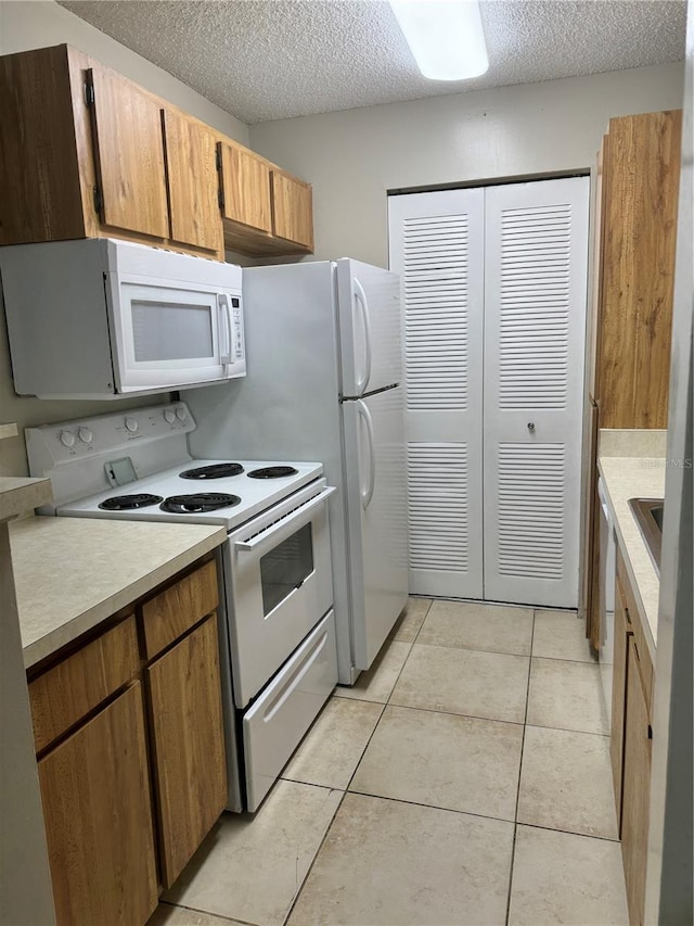 kitchen with a textured ceiling, light tile patterned floors, and white appliances