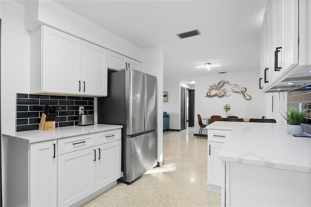 kitchen with stainless steel refrigerator, light stone counters, decorative backsplash, and white cabinetry