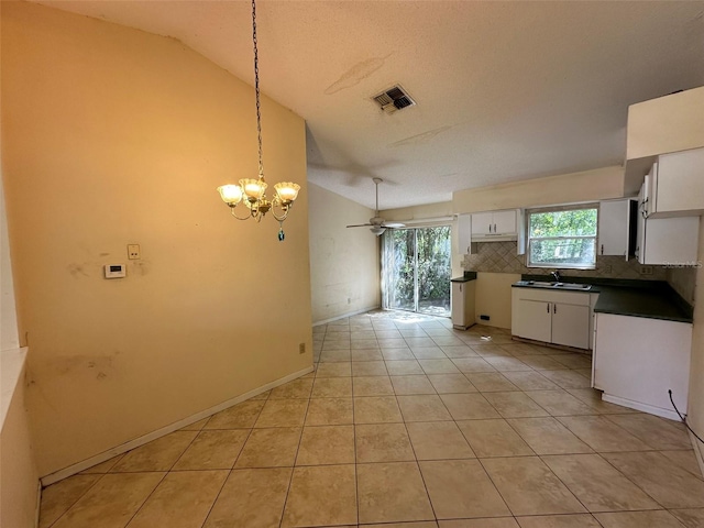 kitchen featuring ceiling fan with notable chandelier, backsplash, light tile patterned floors, lofted ceiling, and white cabinets