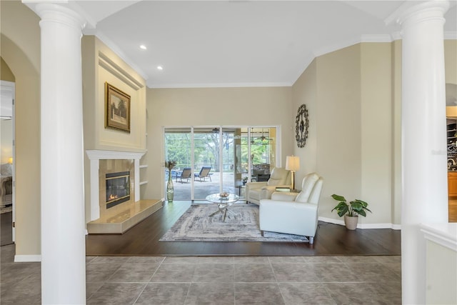 living room featuring a tiled fireplace, dark wood-type flooring, crown molding, and ornate columns