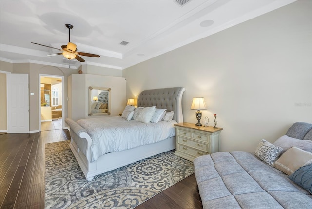 bedroom with a raised ceiling, dark hardwood / wood-style floors, crown molding, ensuite bath, and ceiling fan