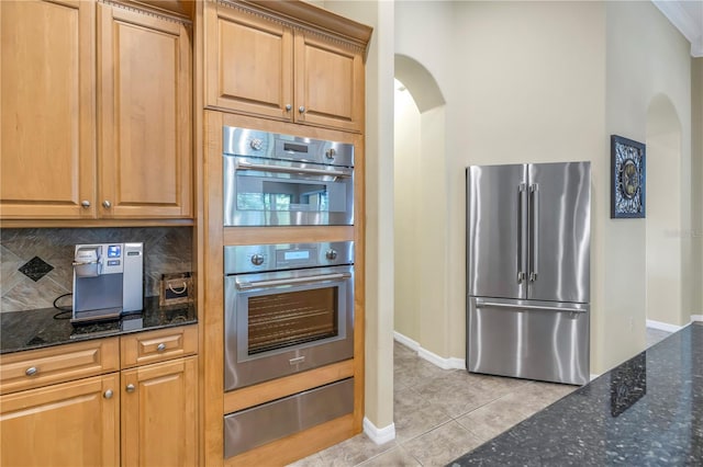 kitchen with stainless steel appliances, dark stone countertops, light tile patterned floors, and backsplash