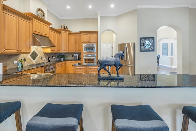 kitchen featuring kitchen peninsula, ornamental molding, appliances with stainless steel finishes, and dark stone counters