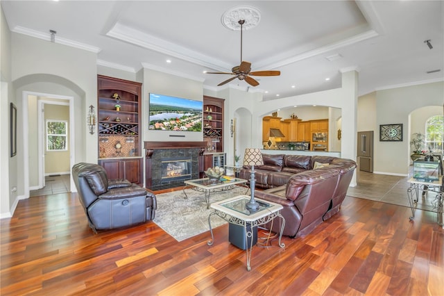 living room with hardwood / wood-style floors, ceiling fan, a raised ceiling, and a high end fireplace