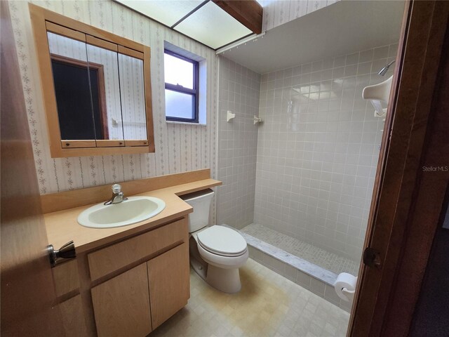 bathroom featuring a tile shower, vanity, and toilet