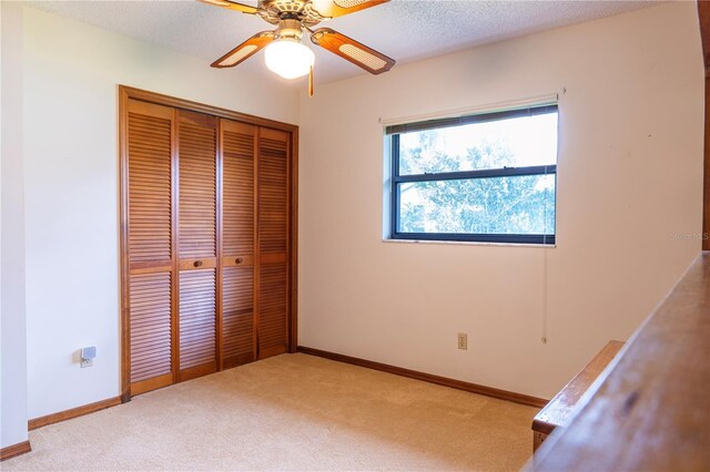 unfurnished bedroom with ceiling fan, light colored carpet, a textured ceiling, and a closet