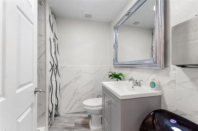 bathroom with a shower, tile walls, toilet, and vanity