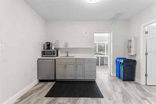 kitchen with gray cabinets, light hardwood / wood-style flooring, stainless steel appliances, and sink