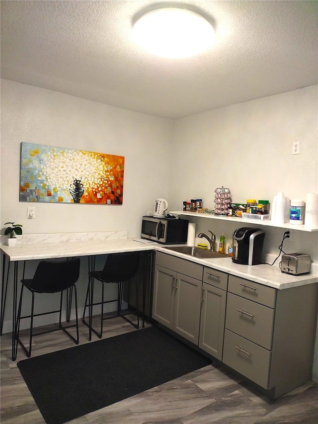 kitchen with gray cabinets, a textured ceiling, a kitchen bar, sink, and dark wood-type flooring