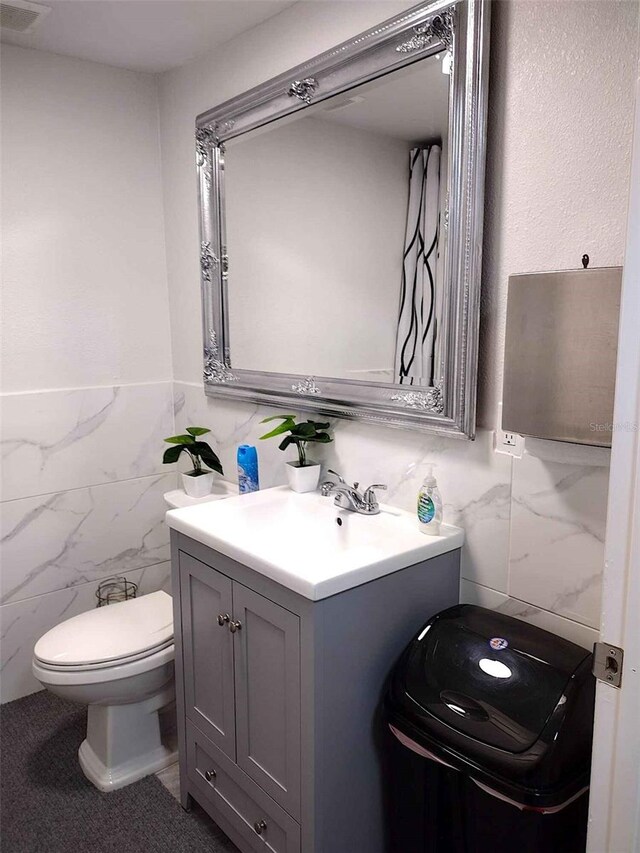 bathroom with vanity, toilet, and tile walls