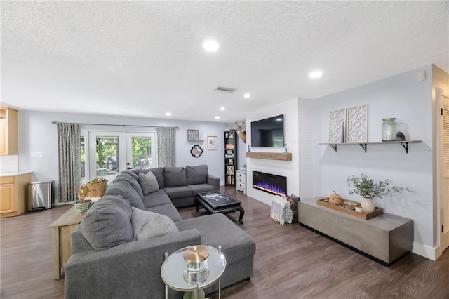 living room featuring french doors, a large fireplace, wood-type flooring, and a textured ceiling