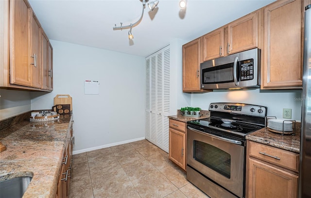 kitchen with light tile patterned floors, rail lighting, stainless steel appliances, and stone countertops