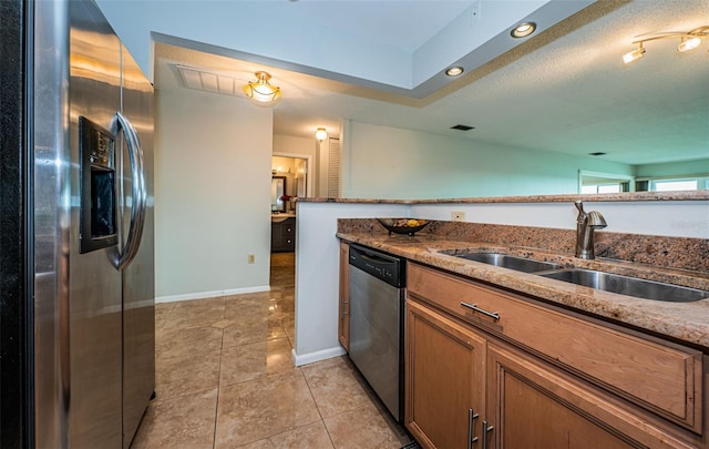 kitchen with a textured ceiling, stainless steel appliances, sink, stone counters, and light tile patterned flooring