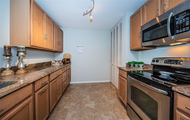 kitchen featuring dark stone countertops, rail lighting, light tile patterned flooring, and appliances with stainless steel finishes