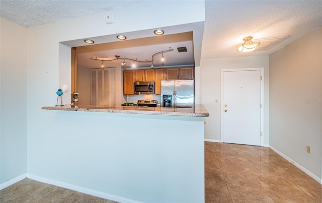 kitchen with kitchen peninsula, light stone countertops, a textured ceiling, and appliances with stainless steel finishes